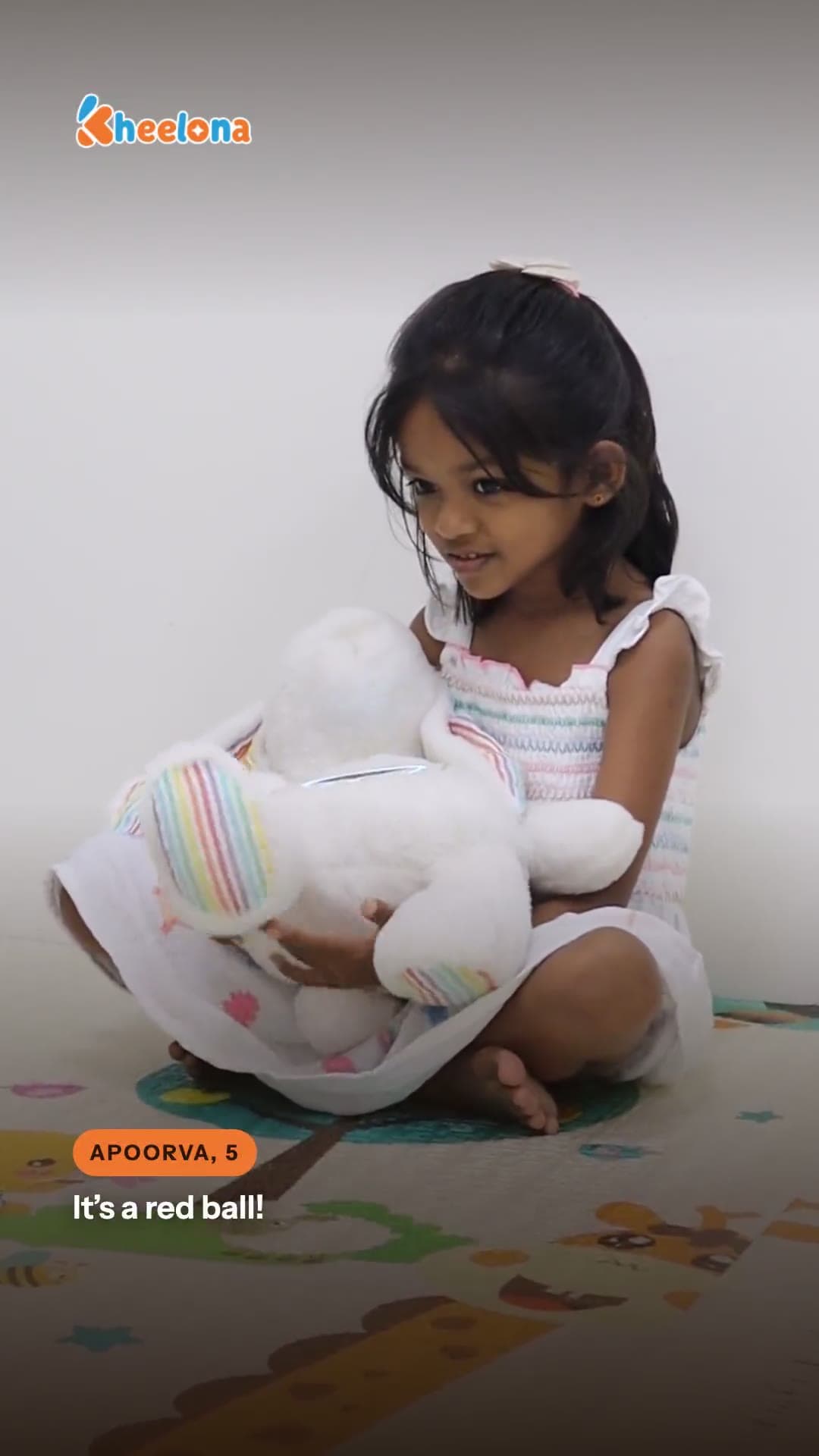 A young girl on a playmat holding the cream Kheelu plush.
